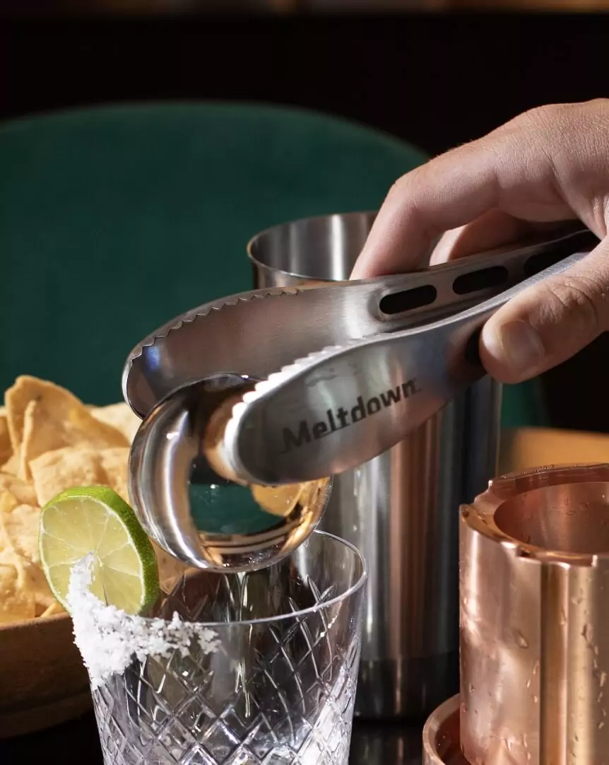 Meltdown Ice steel tongs dropping ice sphere into margarita glass