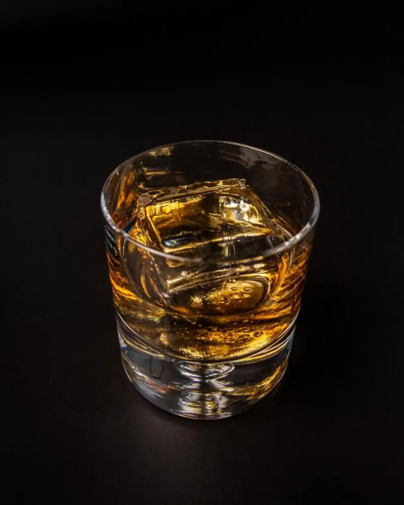 A glass of whiskey with two large ice cubes, set against a dark background.