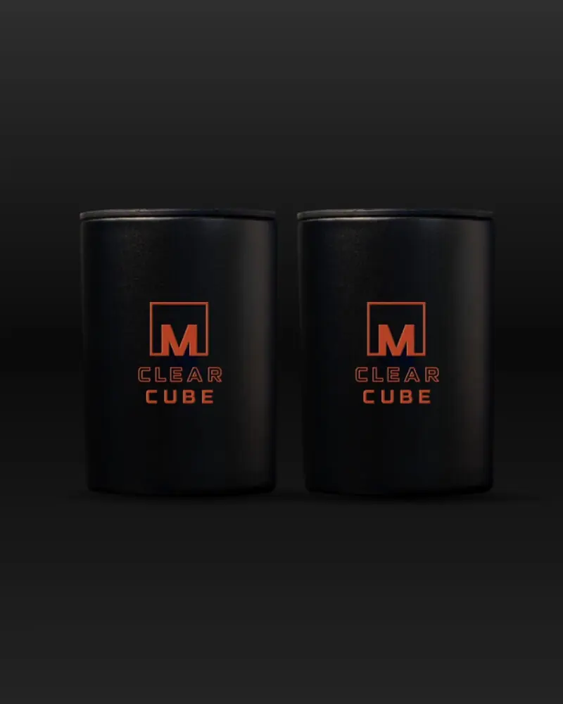Two black cylindrical Meltdown Clear Cube containers, each featuring orange branding, are placed side by side against a dark gradient background. This 2-pack is designed for use with a clear ice maker.