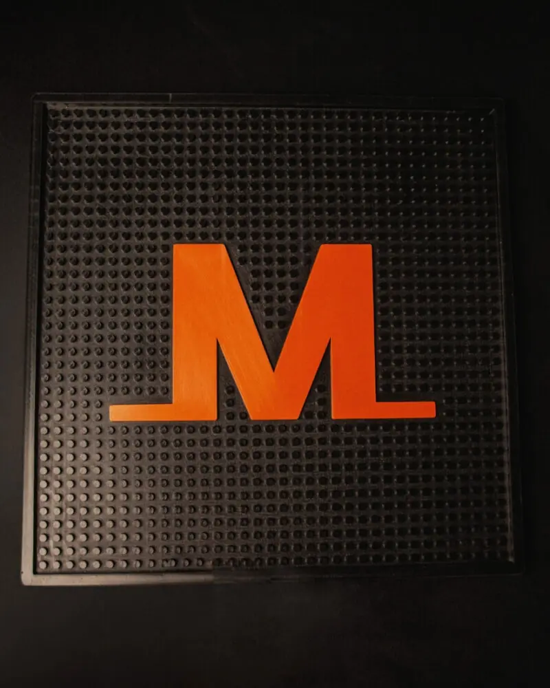 A black textured mat with a large orange letter M in the center, placed on a dark surface.