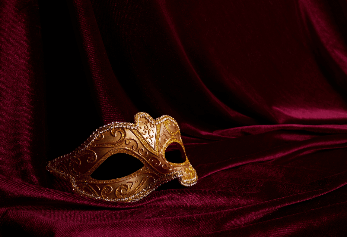A gold, ornate masquerade mask with decorative patterns rests on rich, dark red velvet fabric with elegant folds, setting the perfect mood for an unforgettable party.